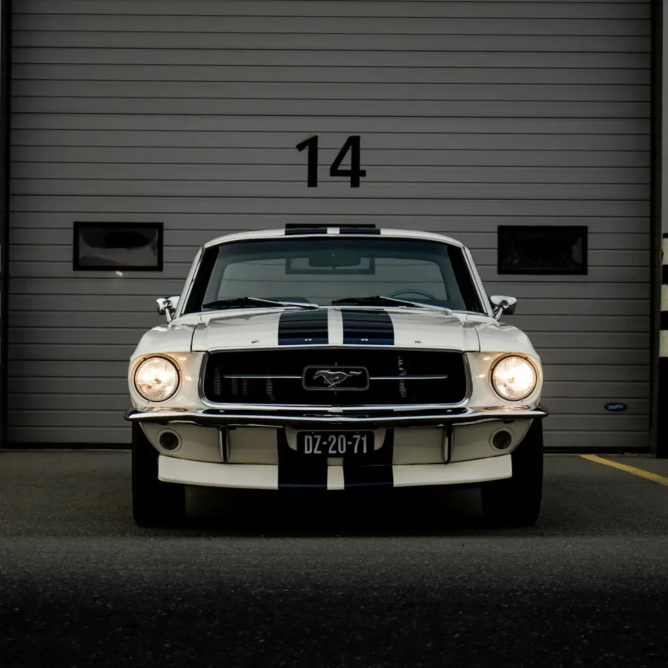 Ford Mustang clásico blanco con franjas azules frente a un garaje